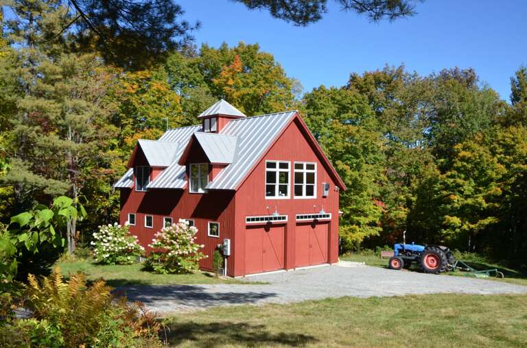 Autumn foliage frames the barn's red exterior and gravel arrival area.