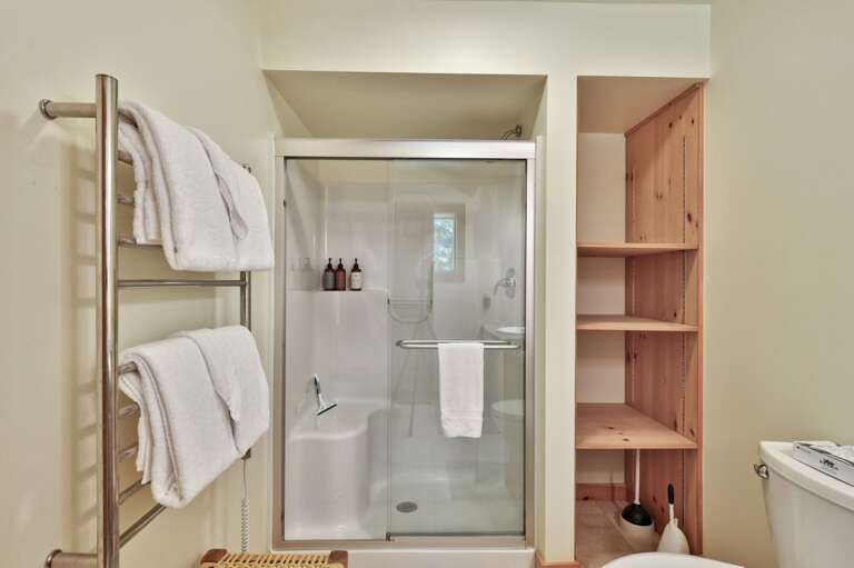 A glass-enclosed walk-in shower and open shelving keep the lower bathroom straightforward and useful.