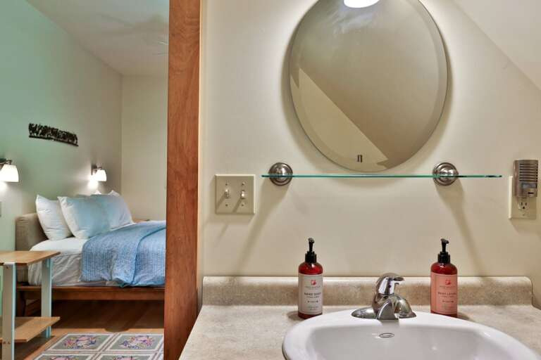 The round mirror and glass shelf keep everyday items organized beside the bedroom.