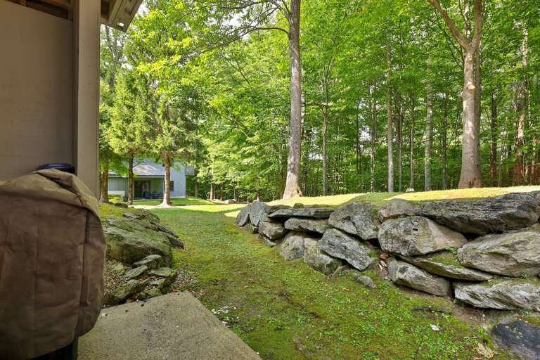 The sheltered patio feels tucked into the landscape, with stone walls and summer greenery all around.