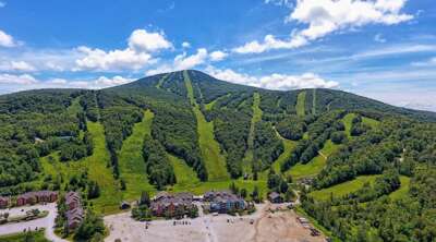 See Pico Mountain beyond ski season, with green trails and the base area spread across the slope.