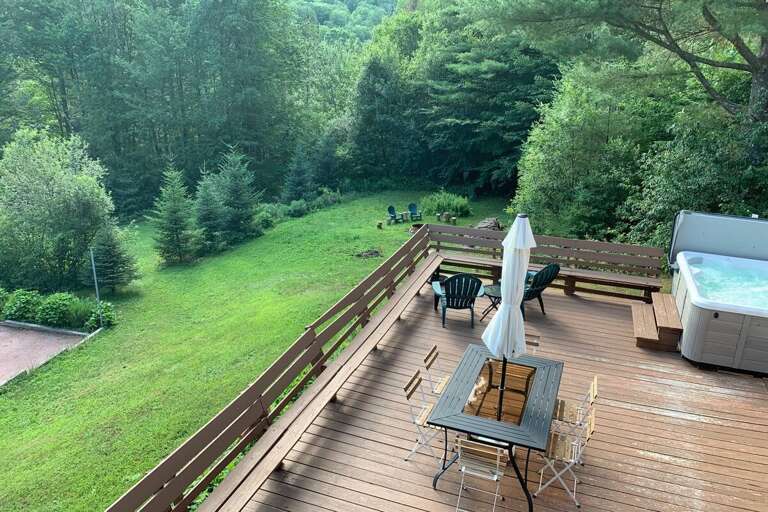 The private six-person hot tub shares the deck with outdoor dining, with the yard just below.