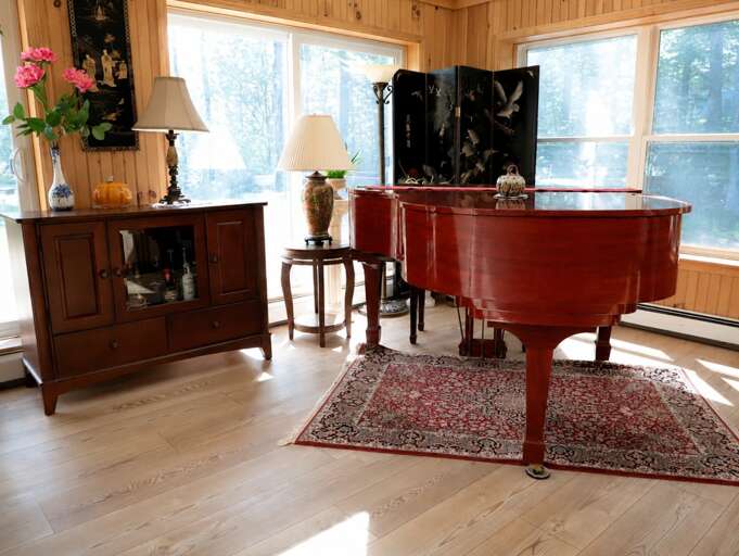 The baby grand piano sits in a wood-paneled corner of the great room, with windows looking into the trees.