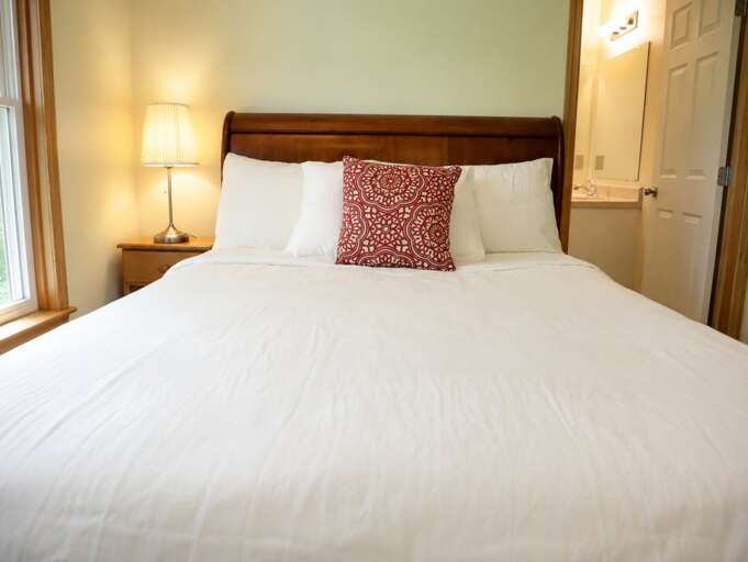 A window beside the bed brings in daylight, with a nightstand and lamp close at hand.