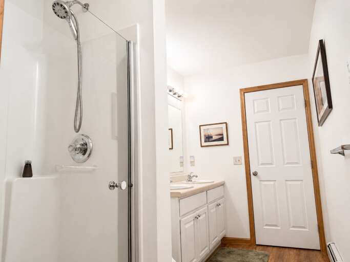 This bathroom has a glass shower door and a handheld showerhead, with the vanity alongside.