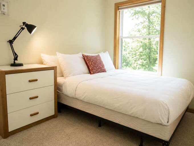 A broad window looks out into the woods, with a dresser beside the bed for unpacking.