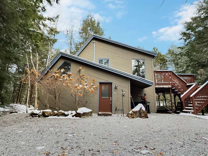 The chalet sits among trees on Toad Road, with an elevated deck and exterior stairs alongside the house.