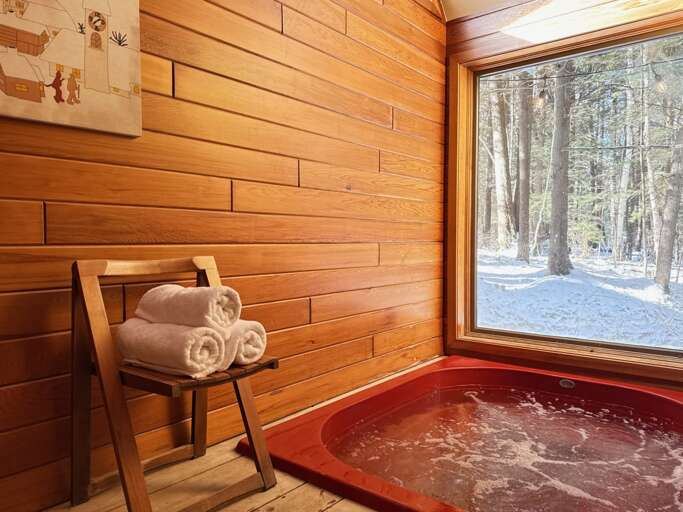 The indoor hot tub faces a large woodland window. Use is included late December through mid-March; off-season setup is $195.