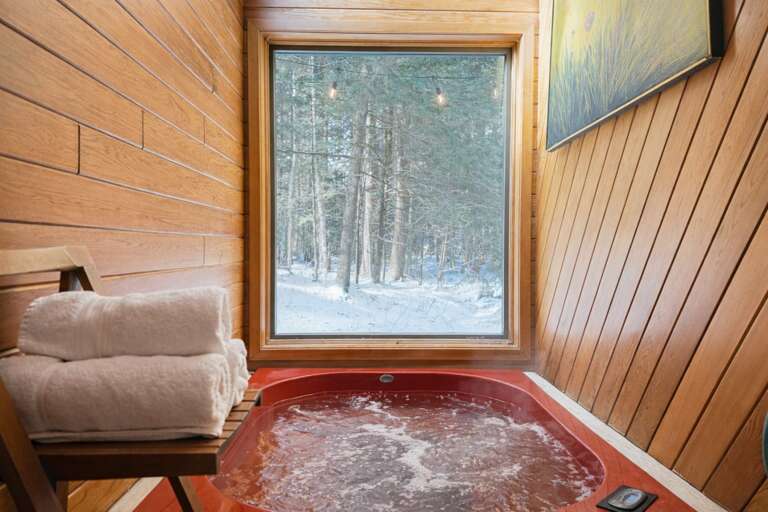 Soak indoors with the woods beyond the window. Hot-tub use is included late December through mid-March; off-season setup is $195.