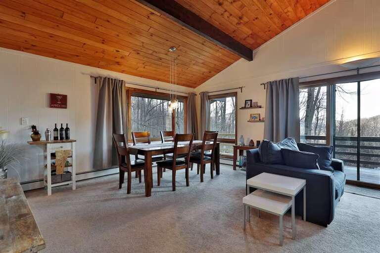 The dining table sits beside corner windows, with the living area just beyond.