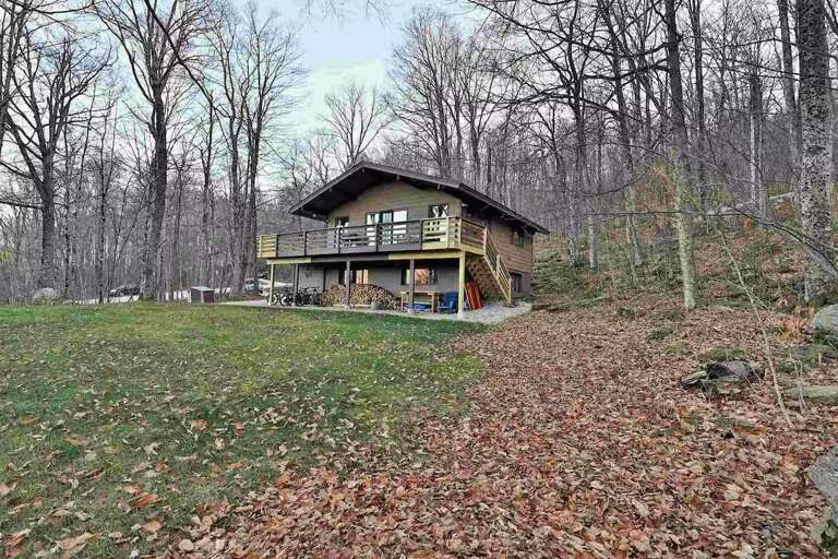 The lawn runs alongside the house, bordered by woodland.