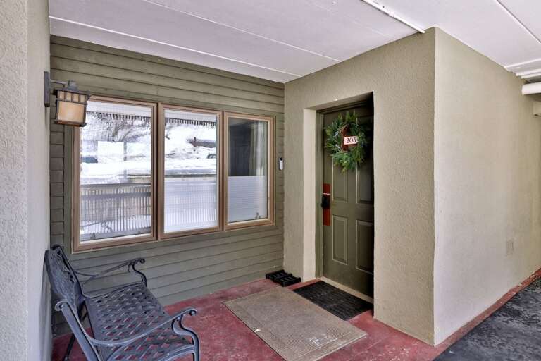 The covered entrance has a bench beside the door marked 205 for a pause while arriving.