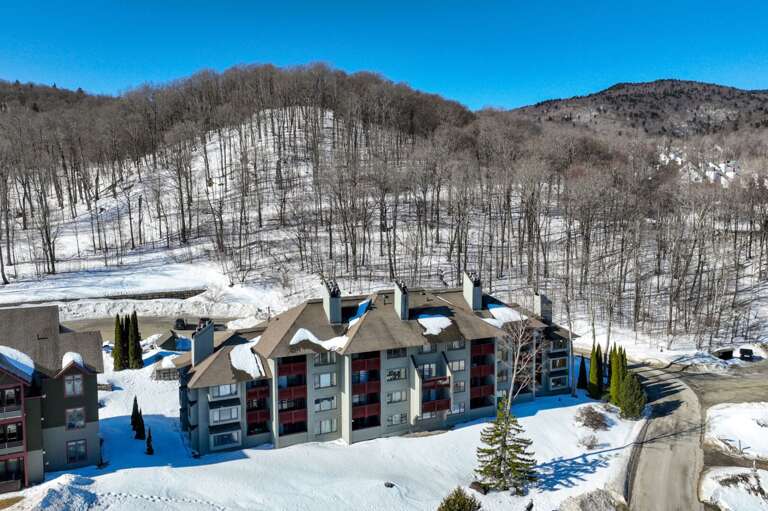 The aerial shows the Cambridge buildings beside a curving road with a snowy, wooded slope behind.