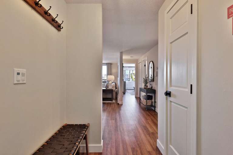 Wall hooks and a bench line the hall before it opens into the living area.