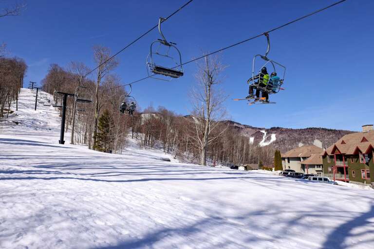 The slope runs beneath the chairlift toward the buildings below, shown on a winter day.