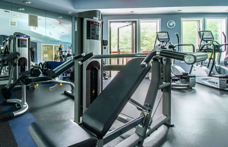 The shared fitness room has weight machines and cardio equipment, with windows along the outside wall.