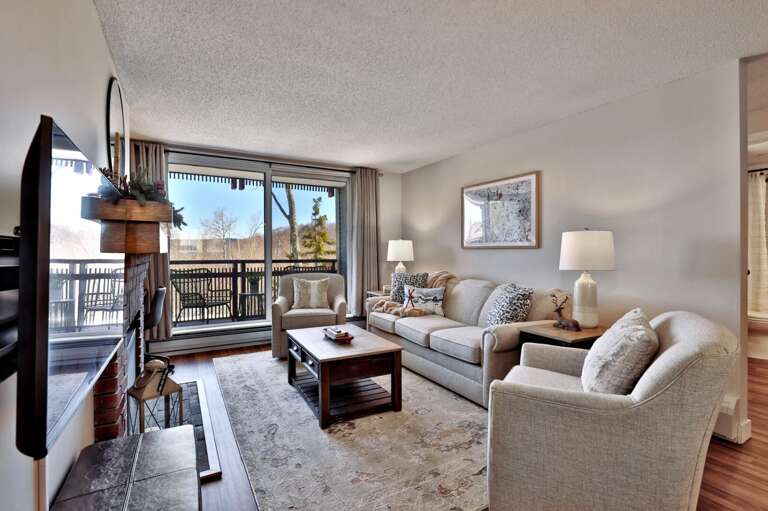 The sofa and armchairs face the TV and fireplace, with the balcony doors bringing the outdoor outlook into the room.