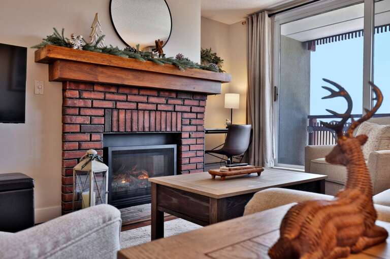 The fireplace is beside the balcony door, so the mountain outlook stays close to the living room.