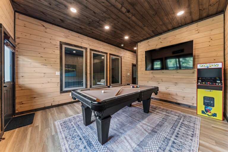 Game room with pool table, arcade machines, and pool view.