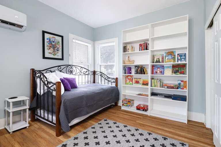 Interior Of A Room With A Bed, Bookshelf, And Rug