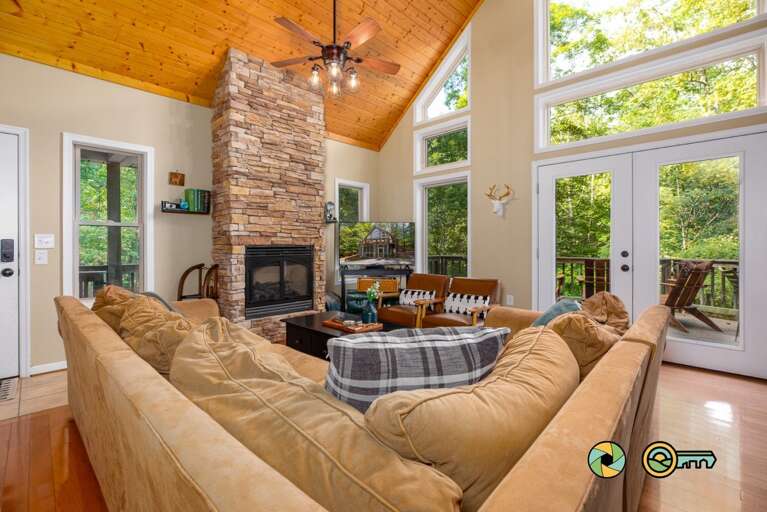 Living Space With Vaulted Ceiling, Central Stone Fireplace, And Forest-framed Glass Doors Living Space With Vaulted Ceiling, Central Stone Fireplace, And Forest-framed Glass Doors