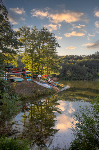 Lake With Stacked Colorful Kayaks And Trees At Sunset