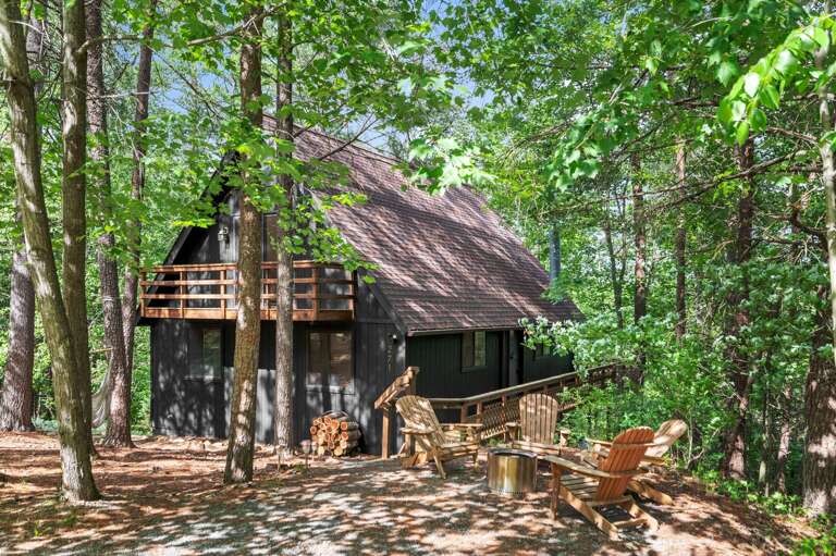 Secluded Cabin Nestled Among Lush, Leafy Trees With Wooden Chairs On A Sun-dappled Clearing