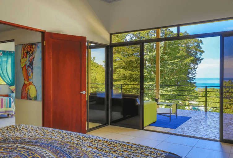 Room Interior With Bed, Artwork, And Sliding Glass Doors Opening To A Sea View