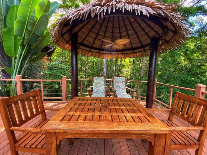 Wooden Patio Furniture Under Thatched Gazebo With Tropical Backdrop