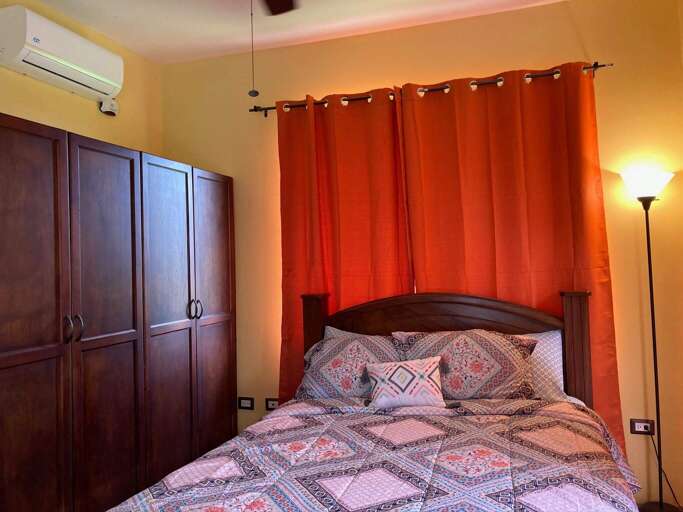 Bedroom With Red Curtains, Patterned Bedspread, And Wooden Furniture