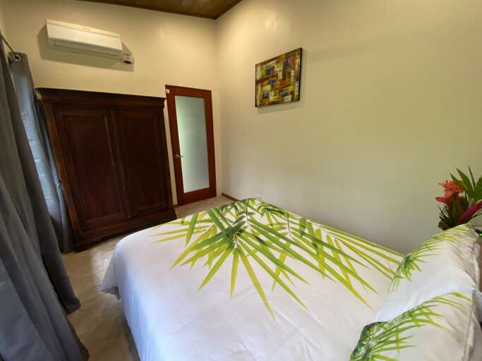 Bedroom With White Bedding And Palm Leaf Pattern, Air Conditioner, And Wooden Door Bedroom With White Bedding And Palm Leaf Pattern, Air Conditioner, And Wooden Door