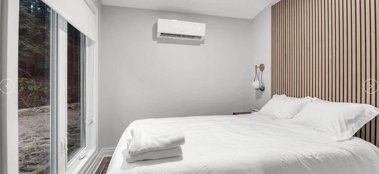 Modern Bedroom With Bed, Wall-mounted AC, And Window View Of Trees