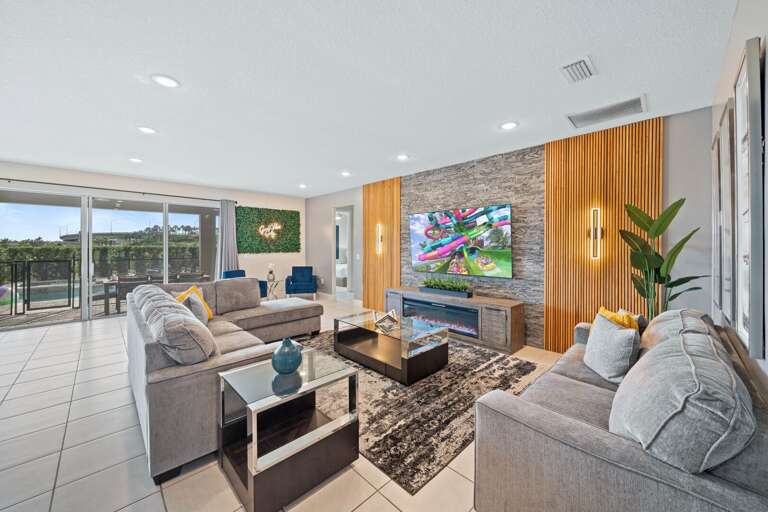 Living area with 86" flat-screen TV, comfy couch, and access to resort-style private pool