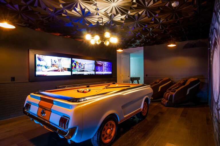Secret agent themed game room with Mustang pool table, shuffleboard, flat screen TVs, and massage chairs