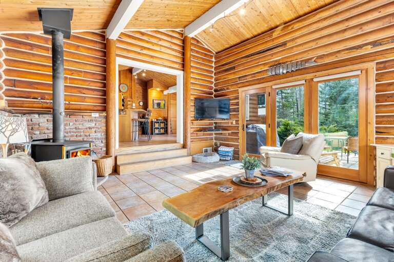 The grand living room space with vaulted ceilings, wood buring fireplace, desk, HDTV with streaming capabilities, french doors to the patio.