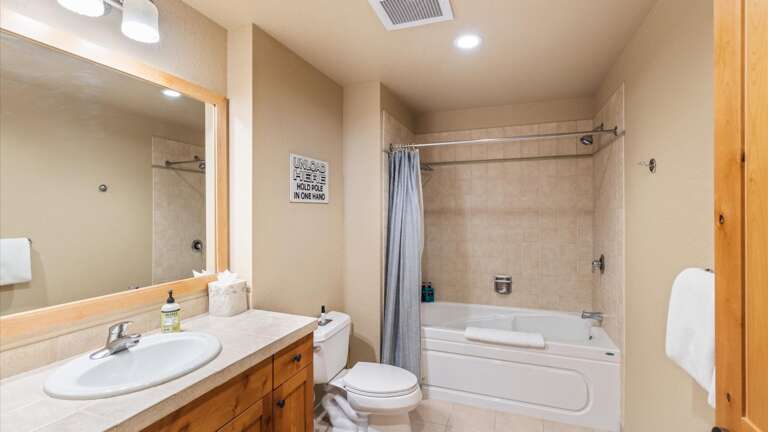 Full size bathroom off the kitchen features a large vanity, toilet, and shower tub combination.