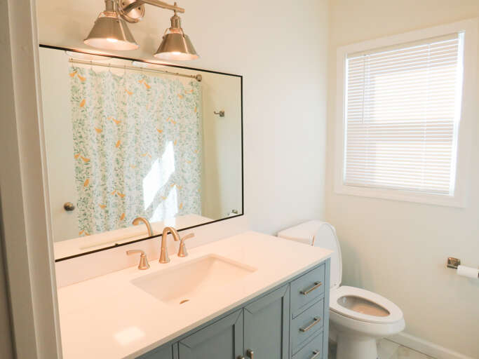Sunlit Bathroom With White Walls, Blue Vanity, And Shower Curtain