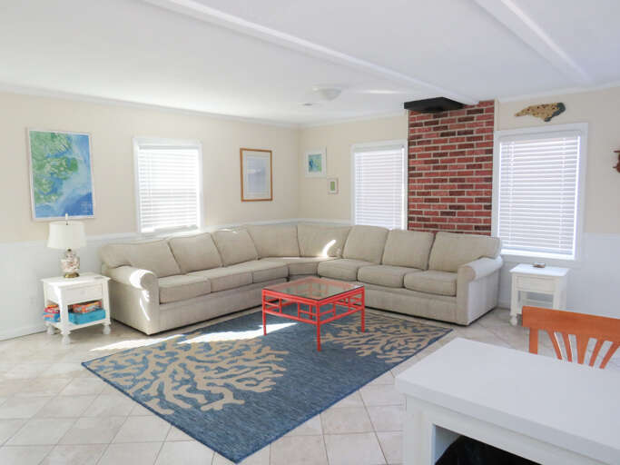 Bright, Breezy Living Space With Large Sectional Sofa, Blue Rug, And Brick Fireplace