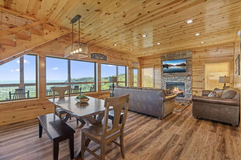 Wood-clad Room With Dining Table, Sofa, And Fireplace Facing Large Windows With View