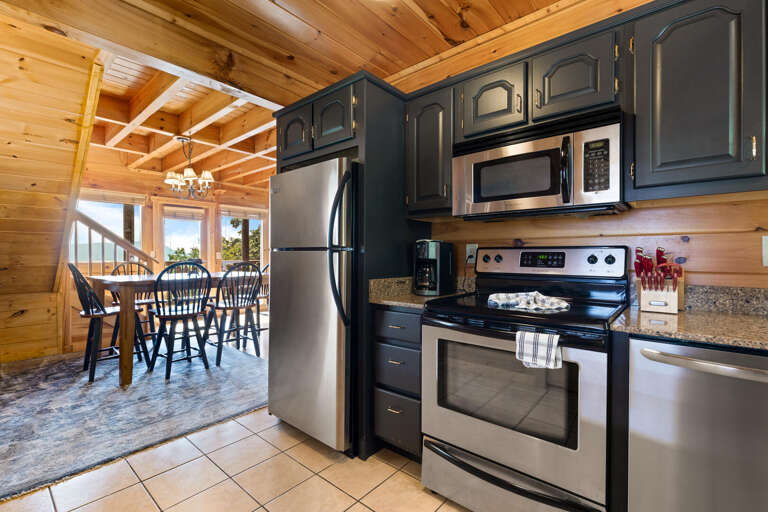 Wooden Cabin Kitchen With Black Cabinets, Stainless Steel Appliances, Leading To Dining Area