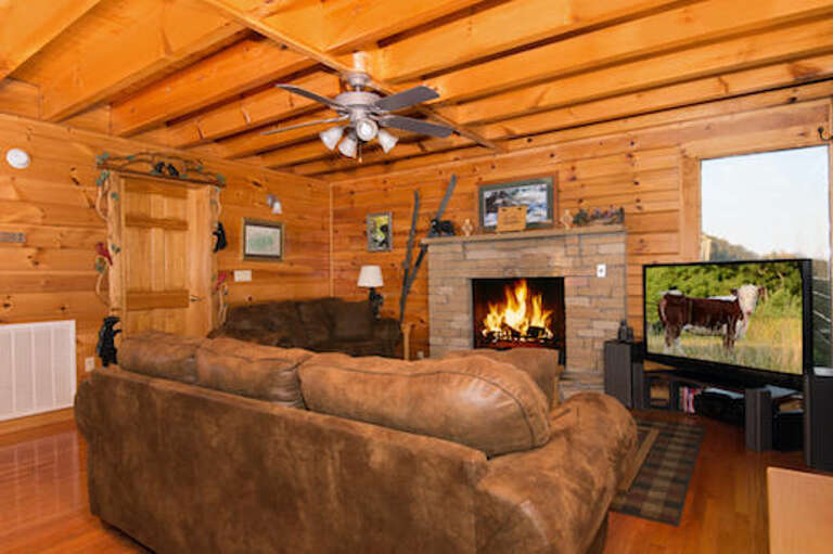 Rustic Room With Roaring Fireplace, Plush Sofa, Paneled Walls, And Pastoral Painting