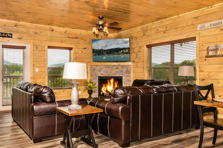 Rustic Room With Roaring Fireplace, Leather Loungers, And A Lake Painting