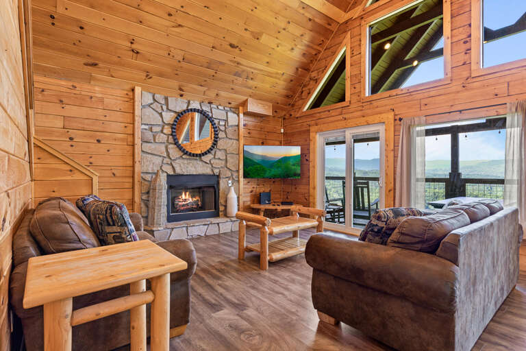 Wood-walled Room With Stone Fireplace, Picture Windows, Plush Sofas, And Timber Table