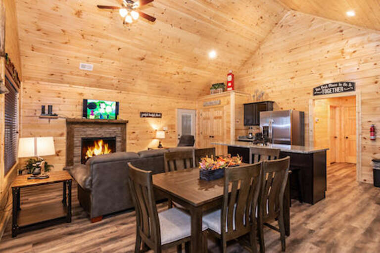 Wood-lined Interior With Fireplace, Dining Set, And Kitchen Appliances