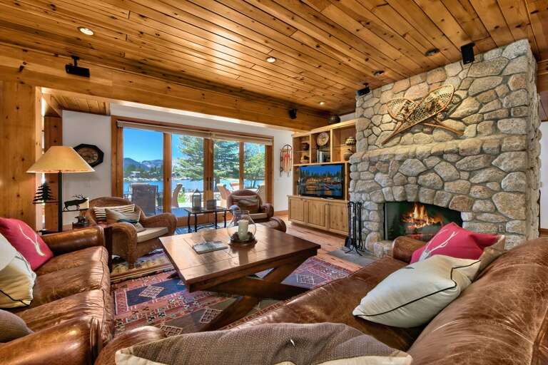 Living area with comfy sofa, flat screen tv, stone encased fireplace, and amazing view of  the lake