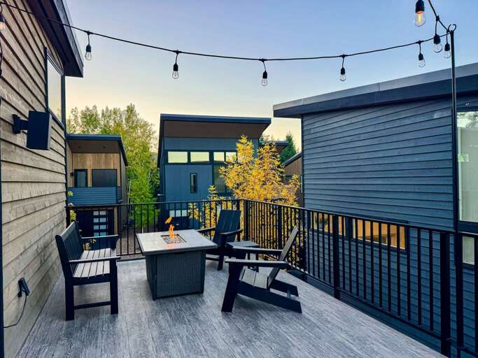 Balcony With Black Railings, Table And Chairs, String Lights, And Trees Beyond