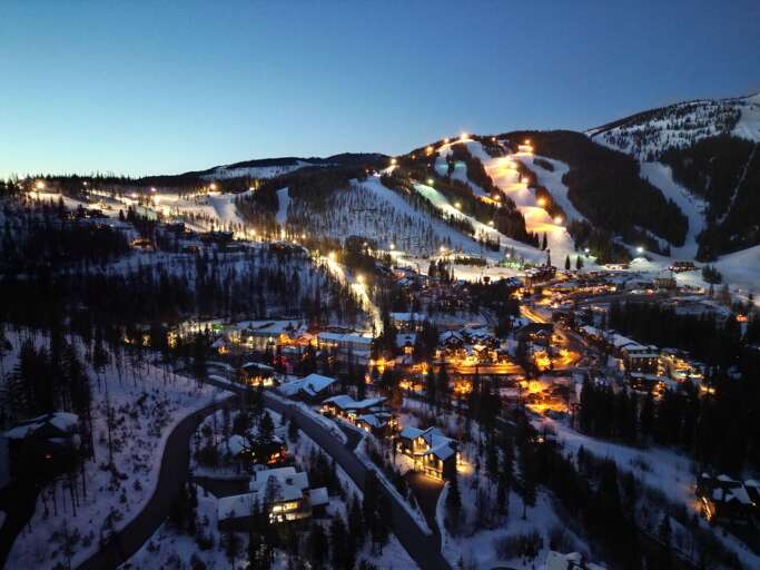 Snowy Slopes Shine Over Serene Village Vista At Dusk