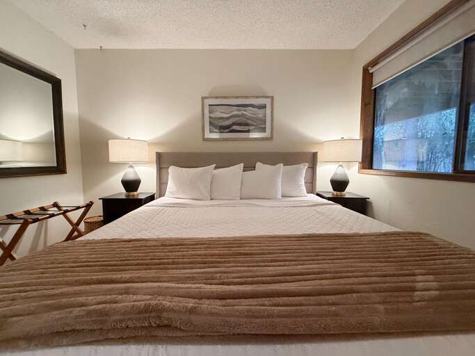 Bed Beneath Bright Beige Blanket, White Wall, Window View
