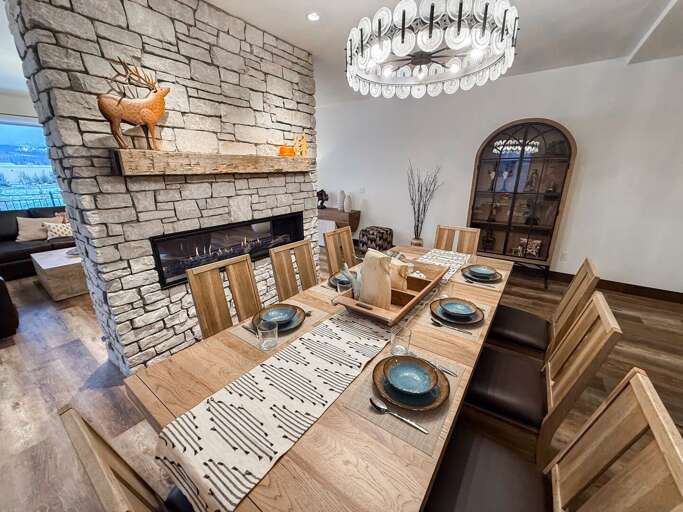 Vacation Rental Dining Space With Stone Fireplace, Wooden Table Set For Dinner, And Elegant Chandelier
