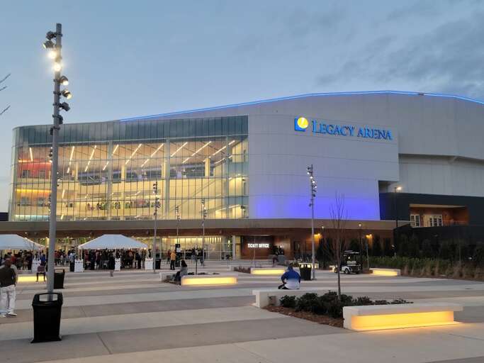 Exterior Of Legacy Arena At Dusk With Illuminated Signage And People Milling Around